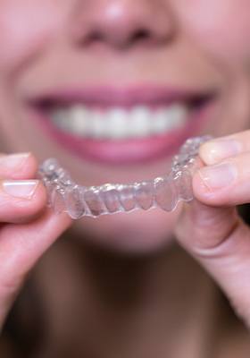 A young woman holding her Invisalign tray in front of her face