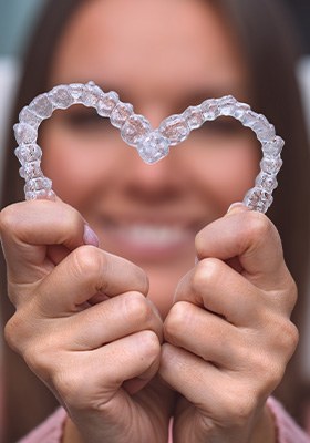 A woman holding her Invisalign trays in the shape of a heart