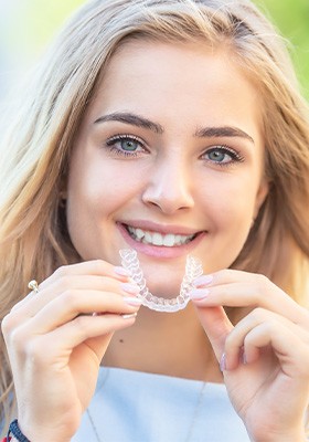 A happy, smiling woman holding an Invisalign tray in front of her