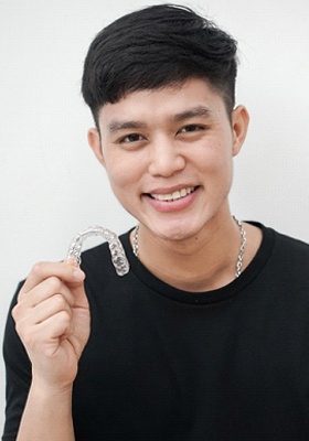 A young, male teen holding a clear aligner