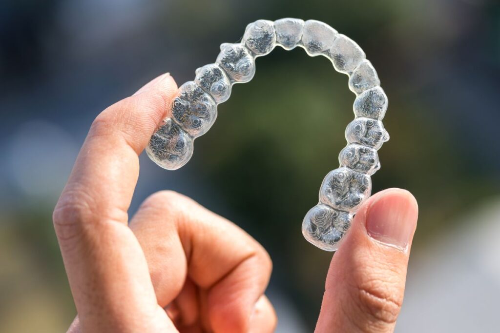 A man's hand holding an Invisalign aligner tray.